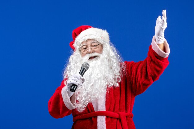 Front view santa claus with red suit and white beard holding mic on blue desk color new year xmas