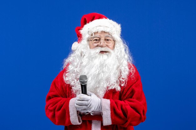 Front view santa claus with red suit and white beard holding mic on blue desk color new year