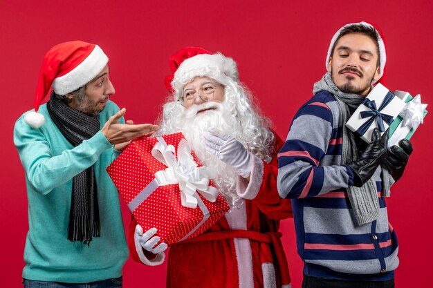 Front view santa claus with two males holding presents on red emotion red new year gift xmas