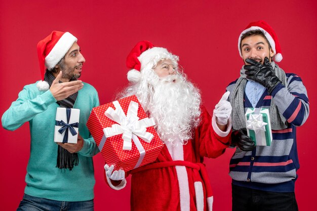 Front view santa claus with two males holding presents on red new year gift emotions christmas red