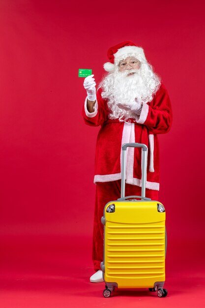 Front view of santa claus with yellow bag holding green bank card on a red wall