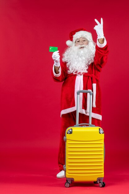Front view of santa claus with yellow bag holding green bank card on red wall