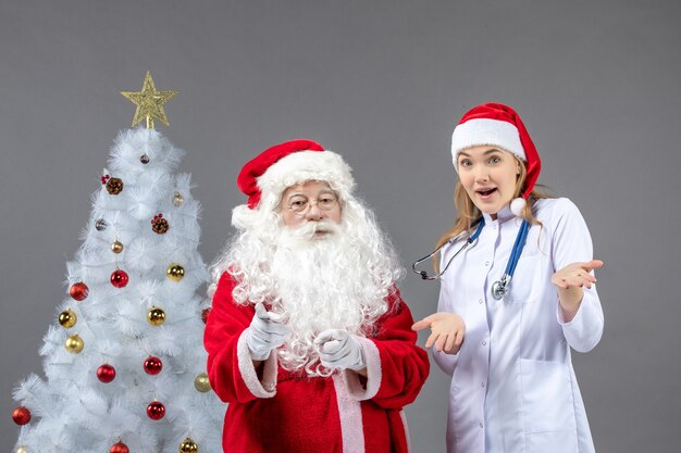 Front view of santa claus with young female doctor on a grey wall