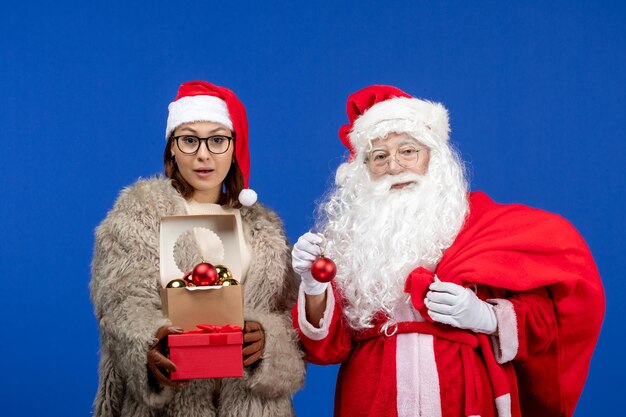 Free photo front view santa claus with young female holding bag with presents and toys on a blue xmas color