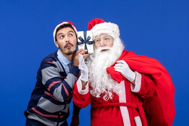 파란색 휴가 선물 크리스마스 색상에 선물로 가득 찬 젊은 남성 가방을 들고 전면 보기 산타 클로스