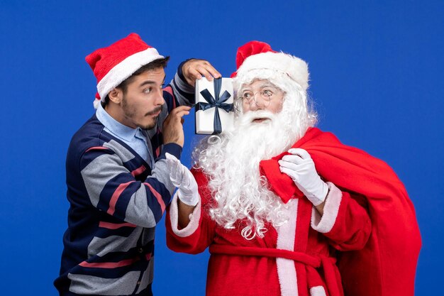 Foto gratuita vista frontale babbo natale con giovane borsa da trasporto maschio piena di regali in vacanza blu presenta il colore di natale