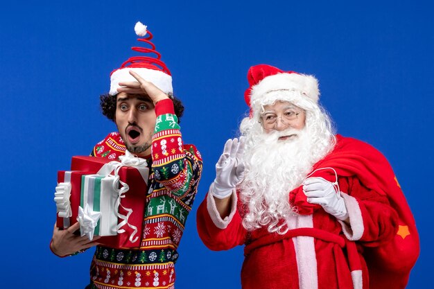 若い男性と青い床の休日の感情のクリスマスの色にさまざまなプレゼントと正面のサンタクロース