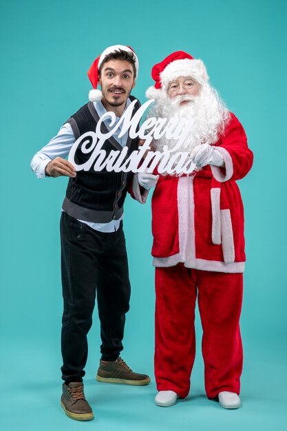 青い背景にメリークリスマスの書き込みを保持している若い男性と正面のサンタクロース