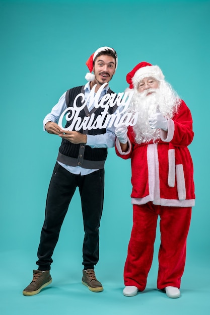 Front view santa claus with young male holding merry christmas writing on the blue background