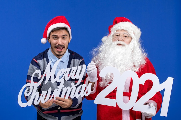 無料Photo 若い男性が保持している正面図のサンタクロースとブルークリスマスのメリークリスマスの執筆