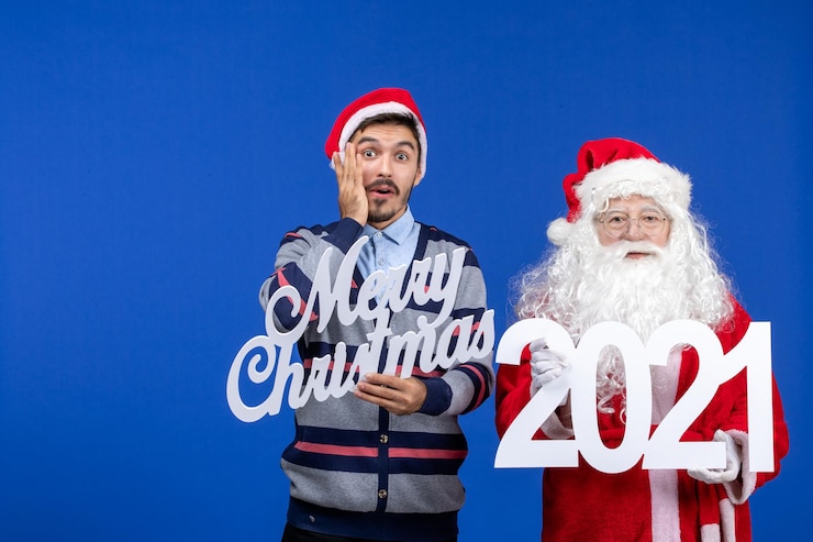 無料Photo 若い男性が保持している正面図のサンタクロースとブルークリスマスのメリークリスマスの執筆