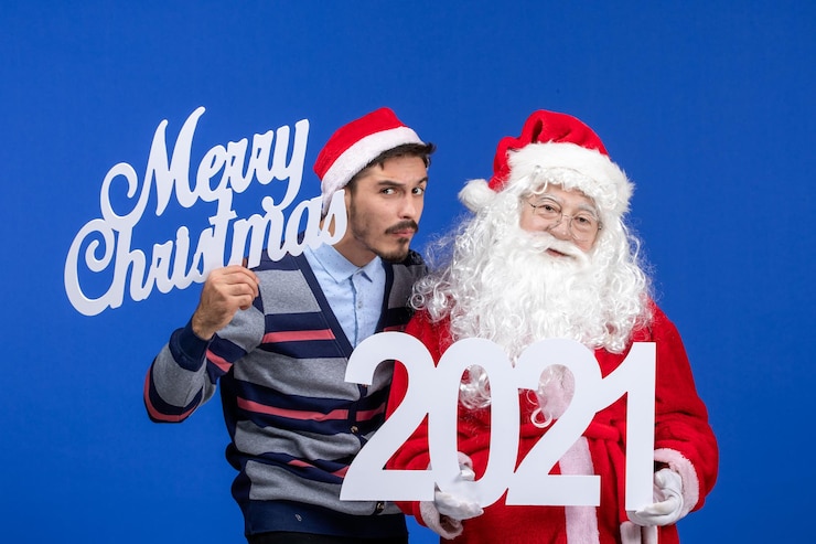 無料Photo 若い男性が保持している正面図のサンタクロースと青い色のメリークリスマスの書き込み