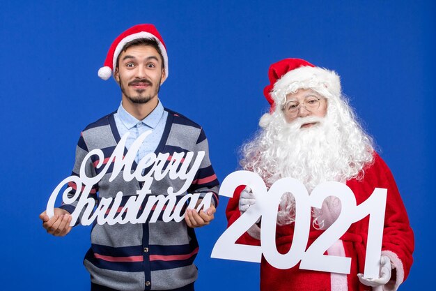 Front view santa claus with young male holding and merry christmas writings on blue xmas holiday