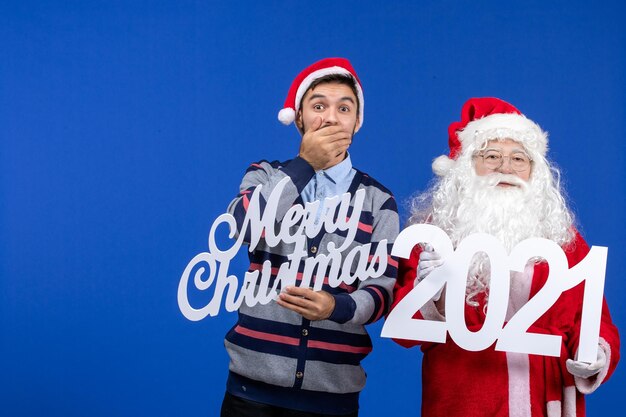 블루 크리스마스 휴일에 젊은 남성이 들고 메리 크리스마스 글과 함께 전면 보기 산타 클로스