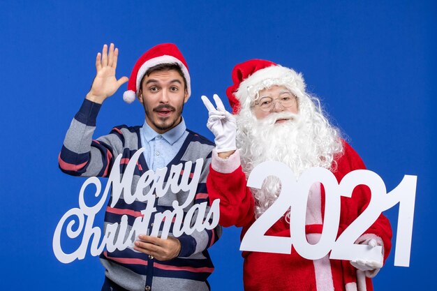 Вид спереди санта-клауса с молодым мужчиной в руках и веселыми рождественскими надписями на синем