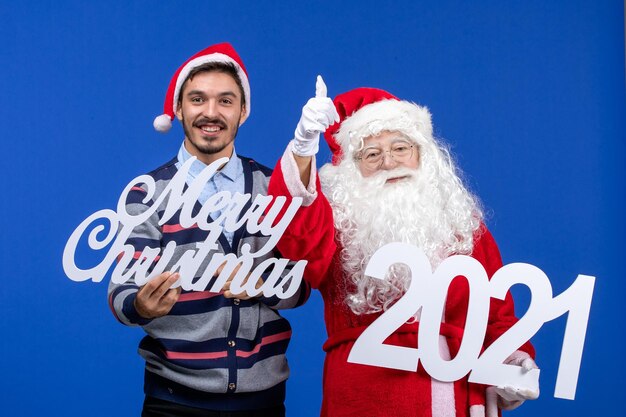 Front view santa claus with young male holding and merry christmas writings on blue