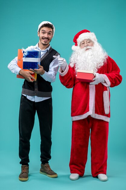 Front view of santa claus with young male and presents on blue wall