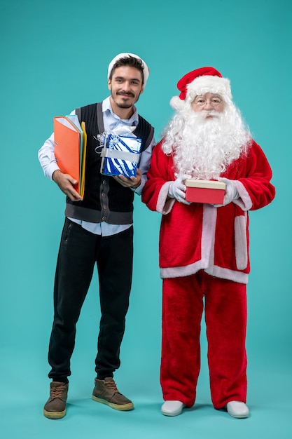 Front view of santa claus with young male and presents on blue wall