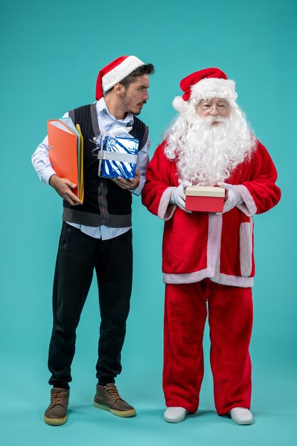 Front view of santa claus with young male and presents on blue wall