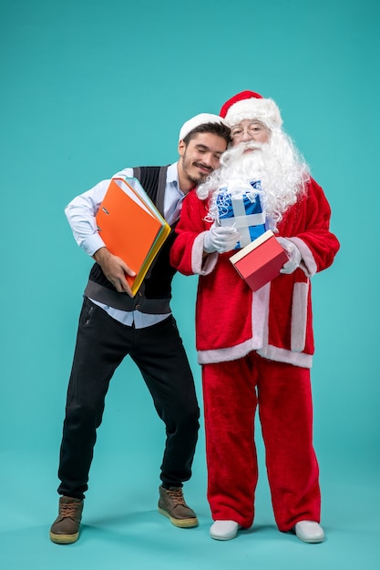 Front view of santa claus with young male and presents on blue wall