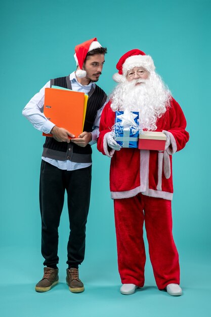 Front view of santa claus with young male and presents on blue wall