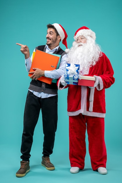 Front view of santa claus with young male and presents on blue wall