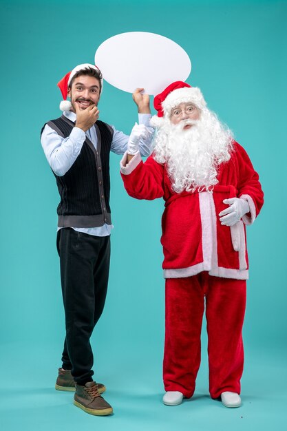 Front view santa claus with young male whos holding white sign on blue floor xmas new year holiday snow color