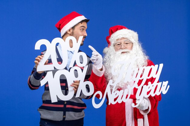 Front view of santa claus with young man holding Happy New Year and numbers writings on blue wall