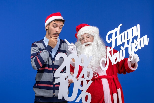 Front view of santa claus with young man holding Happy New Year and numbers writings on blue wall