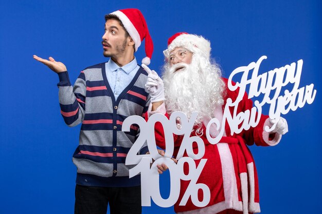 Front view of santa claus with young man holding happy New Year's and percent writings on blue wall