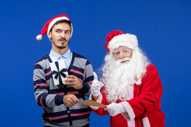 Front view of santa claus with young man holding letter and present on blue wall