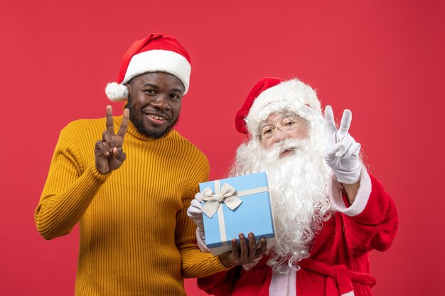 Front view of santa claus with young man holding present on red wall