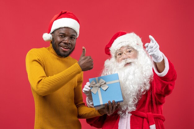 Front view of santa claus with young man holding present on red wall