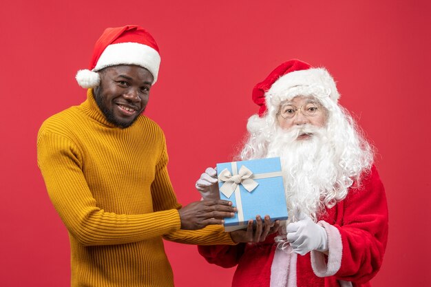 Front view of santa claus with young man holding present on the red wall