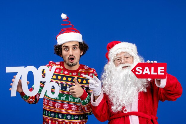 Front view of santa claus with young man holding and sale writings on blue wall