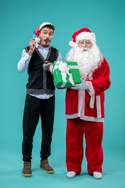 Front view of santa claus with young man and holiday present on a blue wall