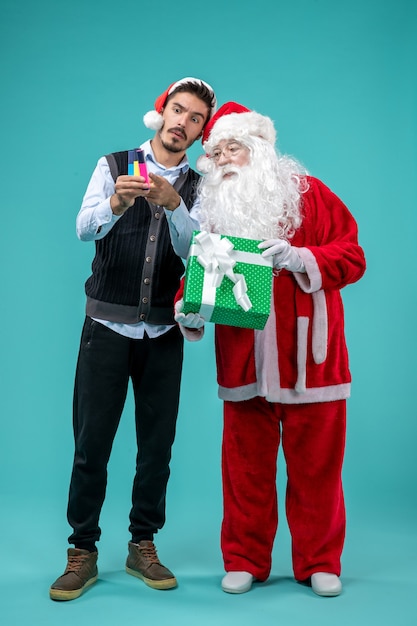 Front view of santa claus with young man and holiday present on a blue wall