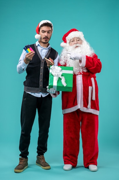 Front view of santa claus with young man and holiday present on blue wall