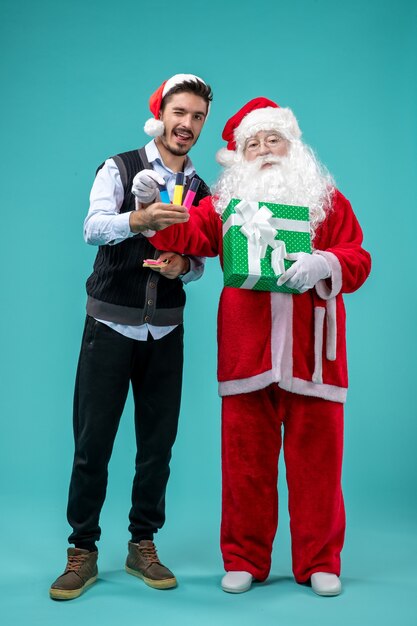 Front view of santa claus with young man and holiday present on blue wall