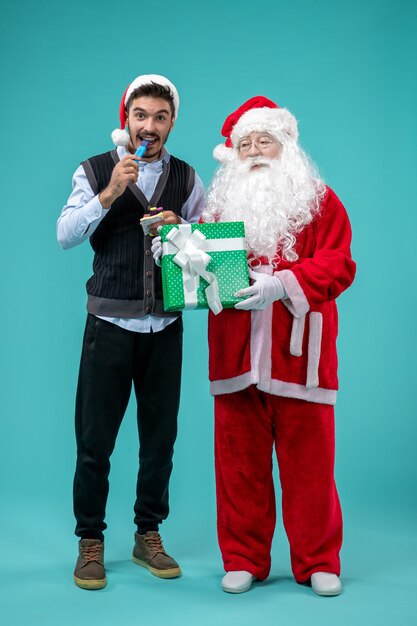 Front view of santa claus with young man and holiday present on blue wall