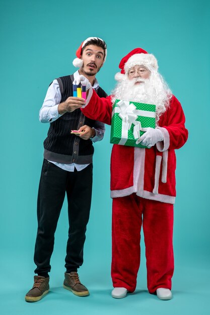 Front view of santa claus with young man and holiday present on blue wall