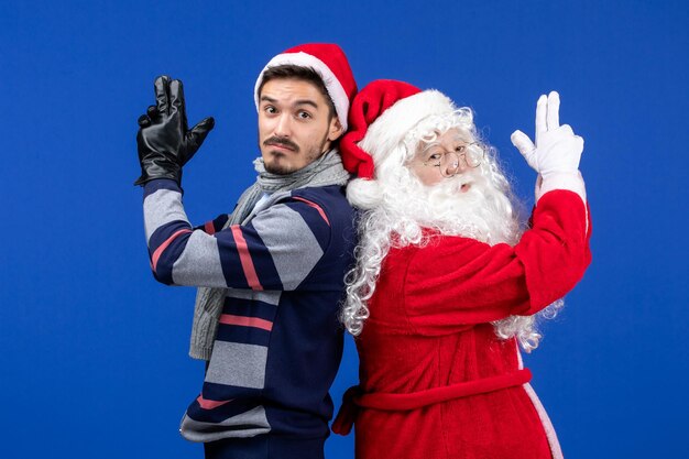 Front view of santa claus with young man posing on blue wall