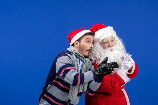 Front view of santa claus with young man posing on the blue wall