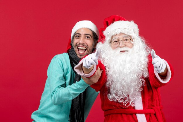 Front view of santa claus with young man posing on a red wall