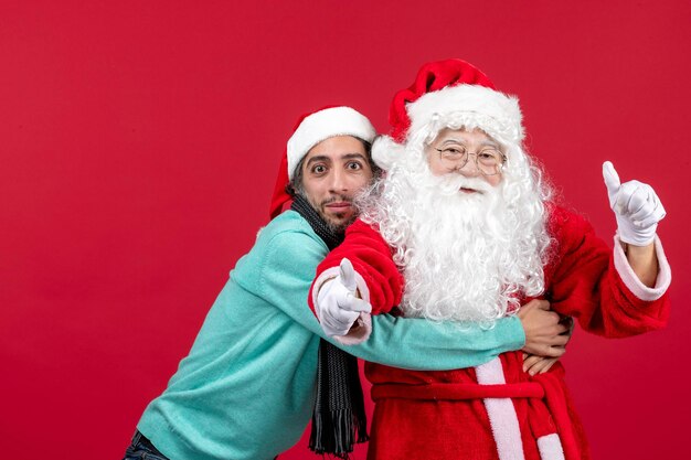 Front view of santa claus with young man posing on the red wall