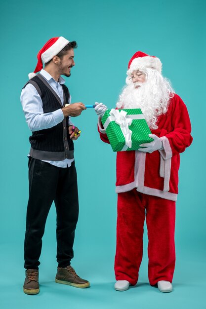 Front view of santa claus with young man and present on blue wall