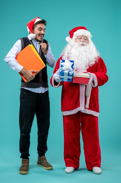 Front view of santa claus with young man and presents on blue wall