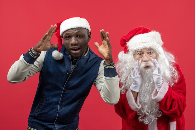 Free photo front view of santa claus with young man on red wall