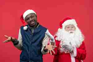 Free photo front view of santa claus with young man on red wall