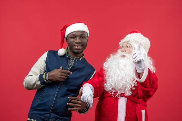 Free photo front view of santa claus with young man on the red wall